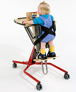 A small child buckled into a red adaptive equipment stander plays with a colorful toy