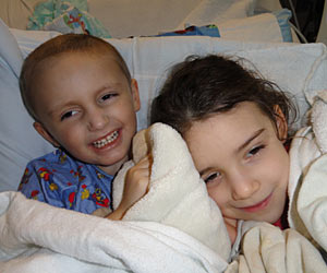 David Bryan, a cancer survivor, smiles as he snuggles in a comfy bed with his sister