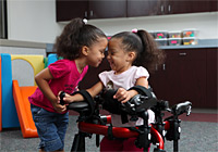 Three year old girl is learning how to walk with a Rifton gait trainer in a classroom setting