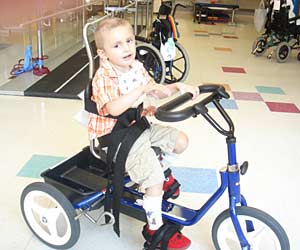 David riding a blue Rifton tricycle at a pediatric cancer survival rehab center
