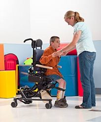 A woman helps a young boy out of his Rifton special needs chair in a colorful playroom setting