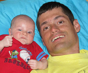A smiling Duane lies on a blue pillow next to his baby nephew.