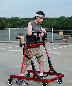 A young man in a Rifton Pacer gait trainer practices ambulation in a parking lot
