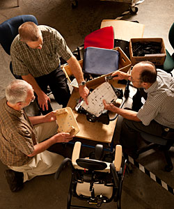 An overhead shot of a team of 3 men gathering at a table to discuss special needs design for a new product 