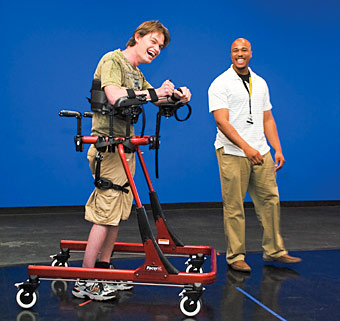A therapist helps guide a young man during neural plasticity rehabilitation as he walks in a gait trainer