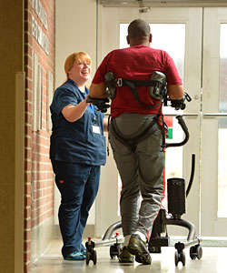 A therapist smiles as she hepls a patient in the ICU using a safe patient handling device, the Rifton TRAM 