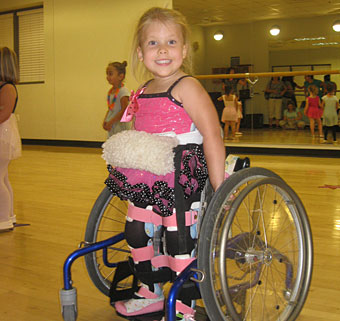 Madi smiles in the studio as she uses her adaptive equipment for dance class