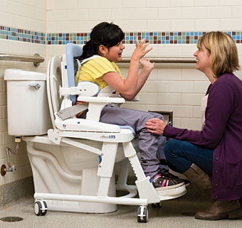 The new Rifton HTS with a child seated in it positioned over a stationary toilet showing an adaptive toilet comparison to the old Rifton Blue Wave Toileting System