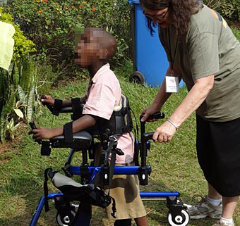 A physical therapist helps a special needs child walk in a used gait trainer device 