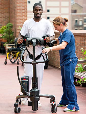 A patient walks in the Rifton TRAM assisted by a caregiver after using it to perform a sit to stand transfer