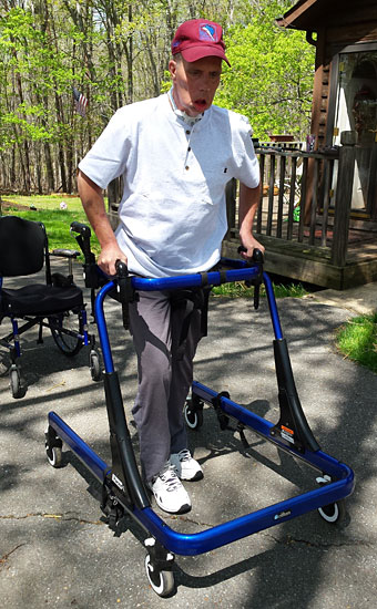 Jimmie Childress in a blue Rifton Pacer gait trainer walking at home.