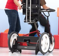 A therapist works with a special needs teen who is pedaling away indoors on a stationary trike