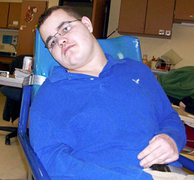 A TBI patient sits slumped down in a wheelchair with limited mobility and control.