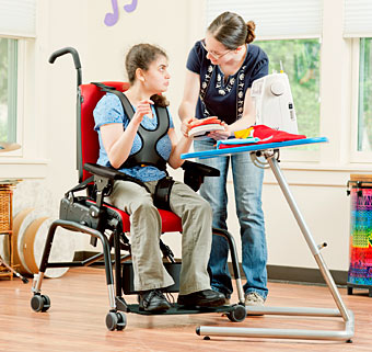 A therapists aids a student using adaptive equipment to practice motor control skills in a classroom setting