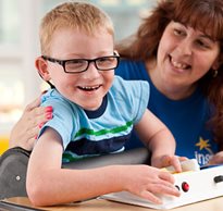 A school therapist helps a smiling young boy with special needs engage in classroom activities 