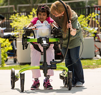 A therapist works with a child with special needs as she practices active movement outdoors in a gait training device