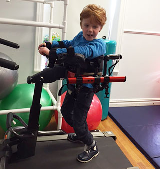 A young boy uses the Dynamic Pacer to practice treadmill gait training with the assitance of his teacher 