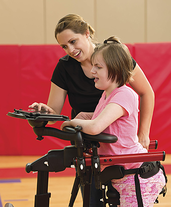 A teacher helps a student in the classroom with functional ambulation using a gait training device to assist her in practicing motor skills