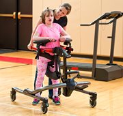 A girl walks in a Rifton Pacer gait trainer, accompanied by a caretaker