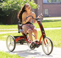 A girl rides on a red Rifton Adaptive Tricycle.