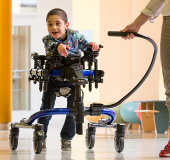 A child walks in a Rifton Pacer walker with a caregiver guiding him.