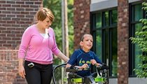 A young woman uses the steering bar on the Rifton Pacer gait trainer to guide the walking of a young boy.