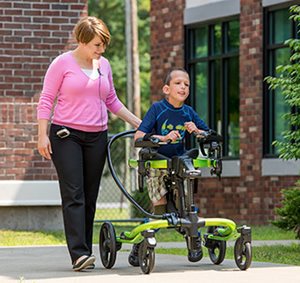 A young woman uses the steering bar on the Rifton Pacer gait trainer to guide the walking of a young boy.