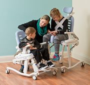 A therapist with two children sitting shower commode chair adjusted to match their special needs.