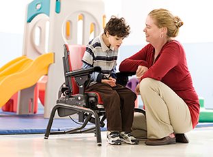 A caregiver has activated the dynamic spring feature on a Standard base Rifton Activity Chair so a child with autism can rock to calm himself