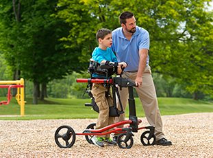 A young boy with his caretaker in a Rifton Pacer gait trainer using the utility base on wood chips.
