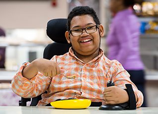 A young boy in a wheelchair using a Rifton Anchor at a school cafeteria table.
