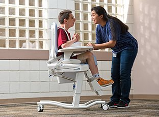 A caregiver positions a school-aged boy in the Rifton HTS adaptive toilet and shower seat.