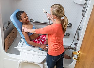 A young woman assists a boy in a Rifton Wave bath chair.