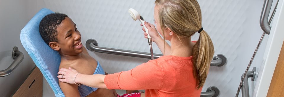 A nurse bathes a school-aged girl using the Rifton Blue Wave Bath Chair to keep her comfortably positioned
