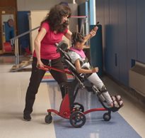 A therapist helps a girl transition to standing in a Rifton Size 1 Stander in supine configuration.