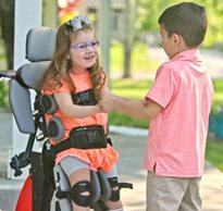A girl stands in a Size 1 Rifton Stander and talks with her brother.