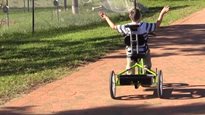 A boy riding on a Rifton Adaptive Tricycle with his hands up in the air